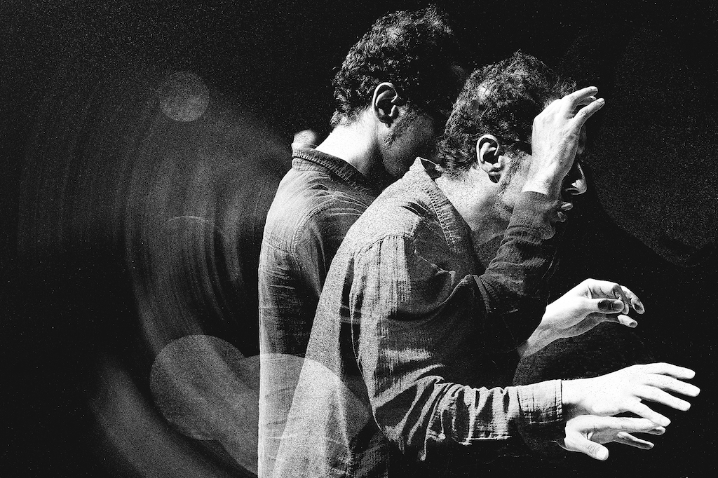 A black and white image shows a man conducting an ensemble sans baton in a dynamic, multi-exposure shot.