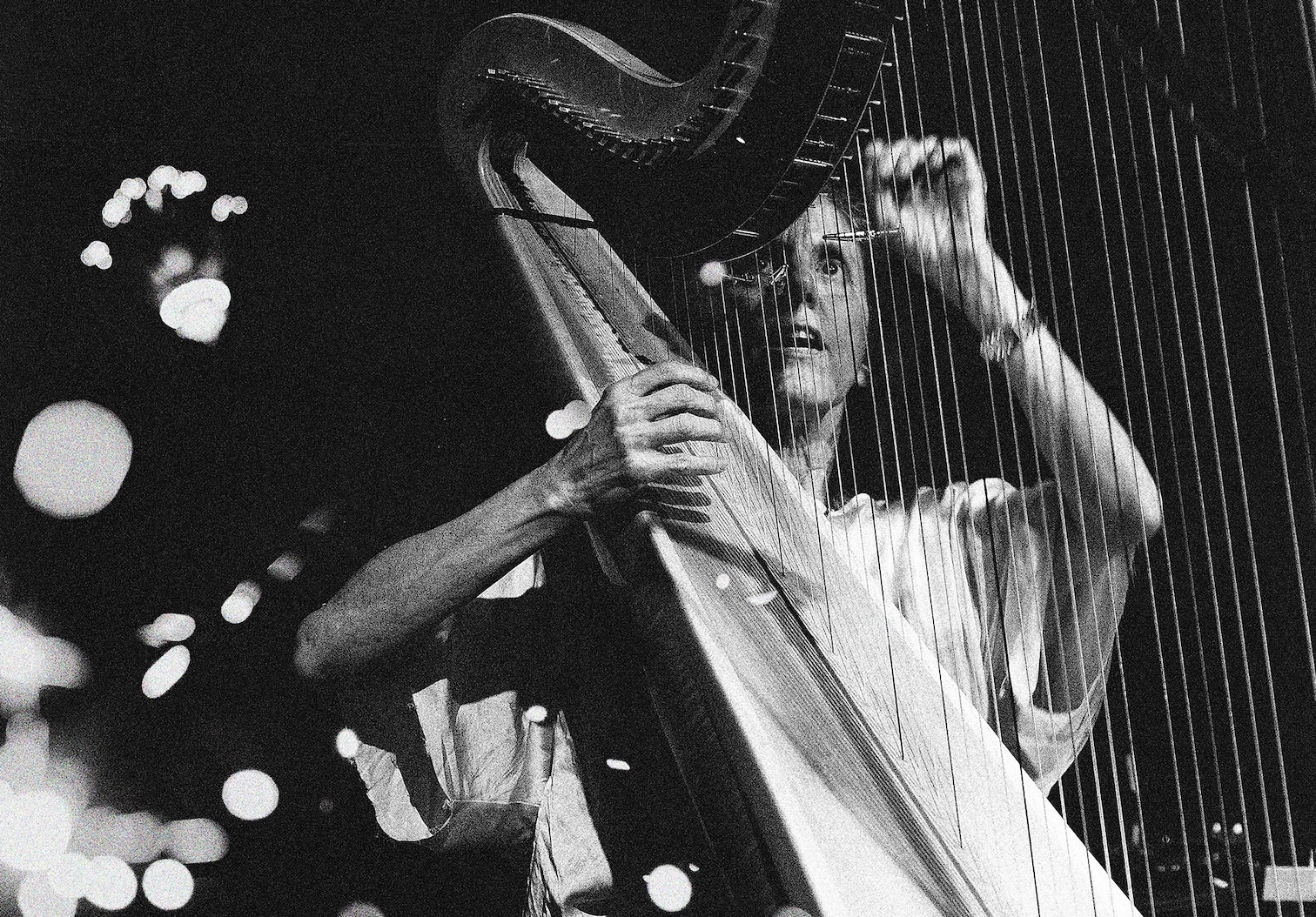 Black and white photo of a focused harpist playing, with bokeh lights in the background. The image conveys a serene and artistic atmosphere.