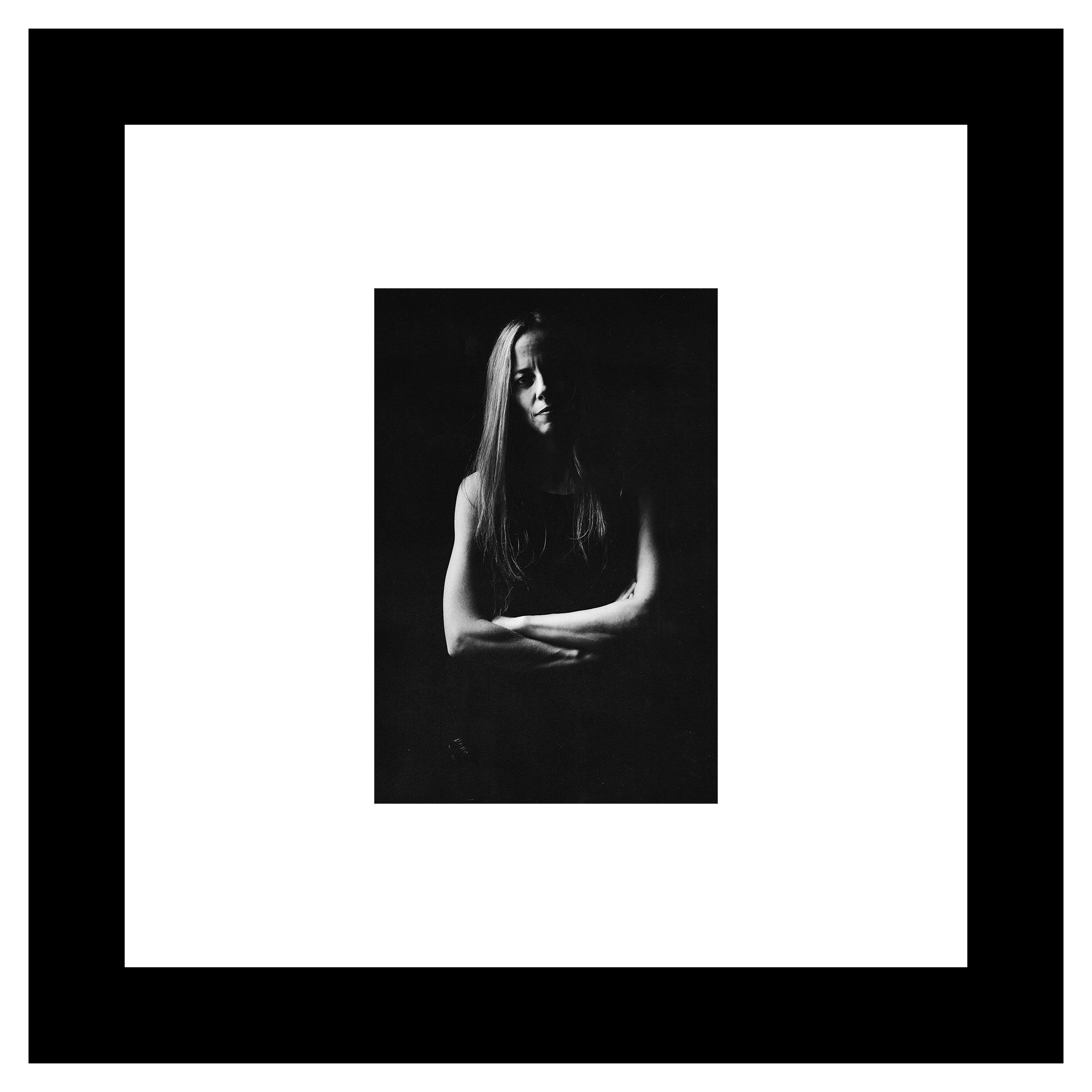 Agustina Crespo portrait. Black and white image of a person with long hair, arms crossed, in soft lighting. The expression is somber and contemplative against a dark background.