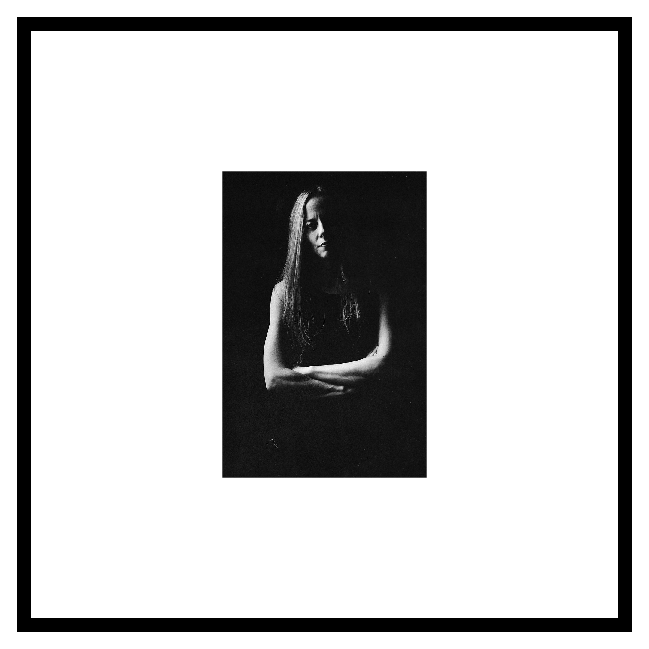 Agustina Crespo portrait. Black and white image of a person with long hair, arms crossed, in soft lighting. The expression is somber and contemplative against a dark background.