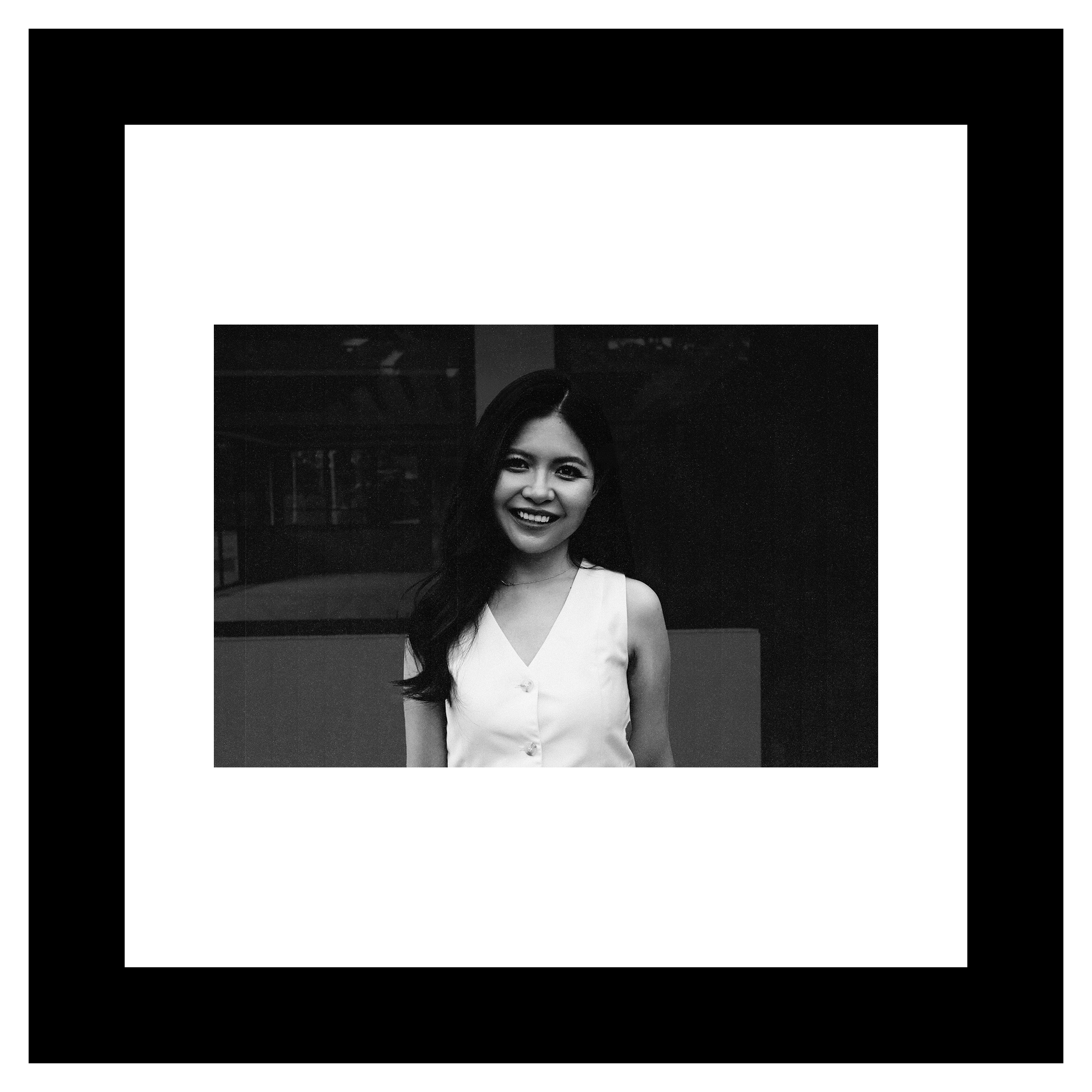 Yuting Tan portrait. Smiling woman in a sleeveless white top against a dark background. Black and white photo, conveying a joyful and serene mood.